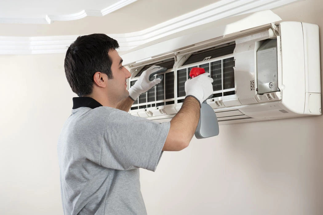 Technician cleaning a wall-mounted AC unit filter at home – What Is The Best Time Of Year To Clean My Air Ducts