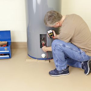 Plumber testing water heater element with analog multimeter.